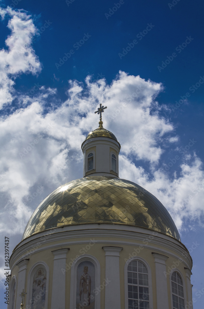 Temple of Orthodox Christians with a gold cupola against a blue sky with white clouds.