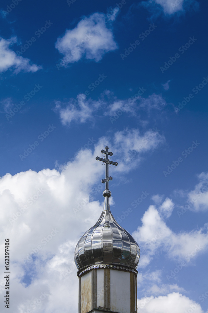 Temple of Orthodox Christians with a silver cupola against a blue sky with white clouds.