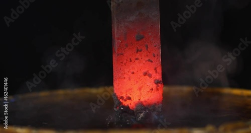  Close-up of blacksmith cooling a iron rod in water at workshop