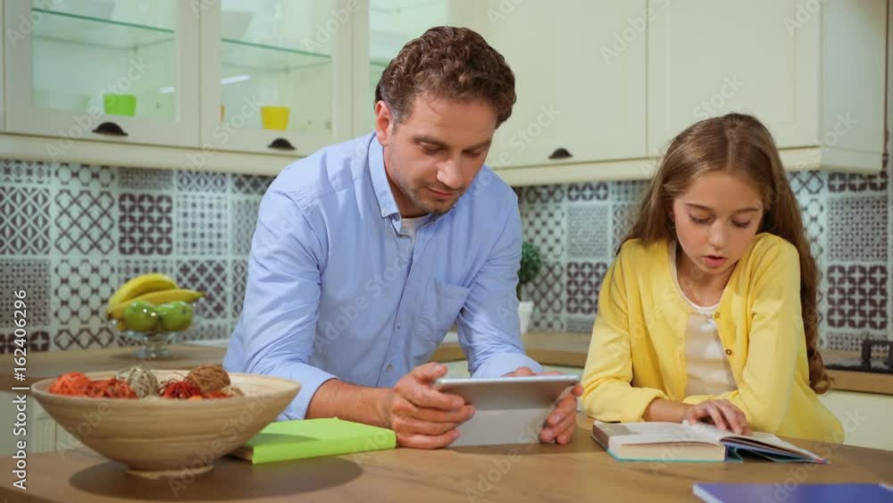 Attractive father helping his daughter with her homework at the kitchen using tablet. Attractive father helping his daughter with her homework at the kitchen using tablet.