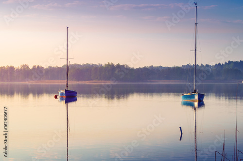 Fototapeta Naklejka Na Ścianę i Meble -  Yachts float on the calm waters of the lake. Early morning. Masuria, Poland .