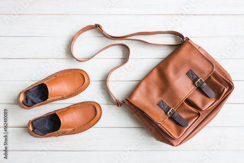 Fashionable concept, men's casual outfits with leather accessories, brown shoes and bag on white wooden board background 