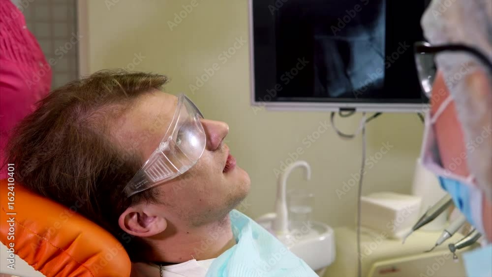Woman dentist and her assistant at work. Doctor polishing patients teeth while assistant using salivary ejector Woman dentist and her assistant at work. Doctor polishing patients teeth while assistant using salivary ejector