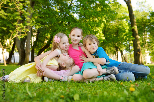 Four cute little children having fun together on the grass on a sunny summer day. Funny kids hanging together outdoors