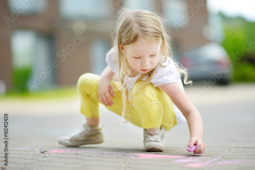 Cute little girl drawing with colorful chalks on a sidewalk. Summer activity for small kids.