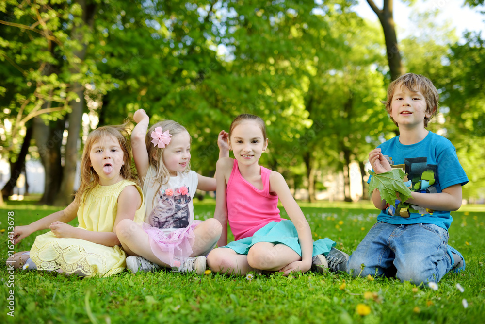 Four cute little children having fun together on the grass on a sunny summer day. Funny kids hanging together outdoors Four cute little children having fun together on the grass on a sunny summer day. Funny kids hanging together outdoors