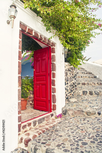 red open door of traditional Greek house with flowers