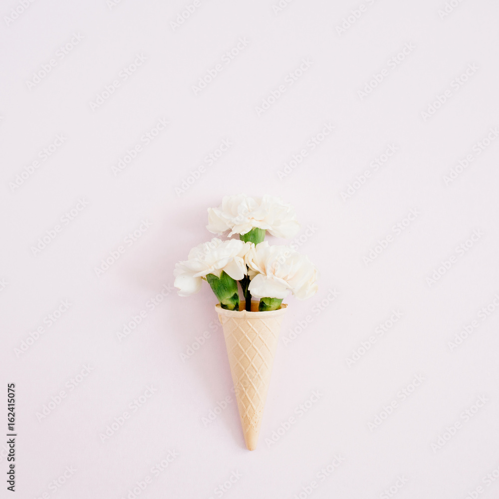 Waffle cone with white carnation bouquet on pale pastel pink background. Flat lay, top view