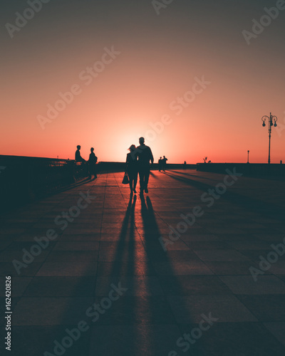 Silhouette di un uomo e una donna abbracciati che camminano in terrazza Mascagni al tramonto photo