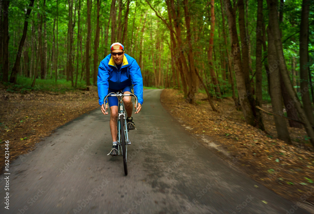 Middle-aged man is riding a road bike along a forest road