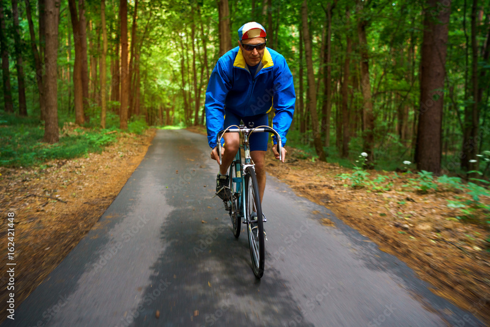 Middle-aged man is riding a road bike along a forest road