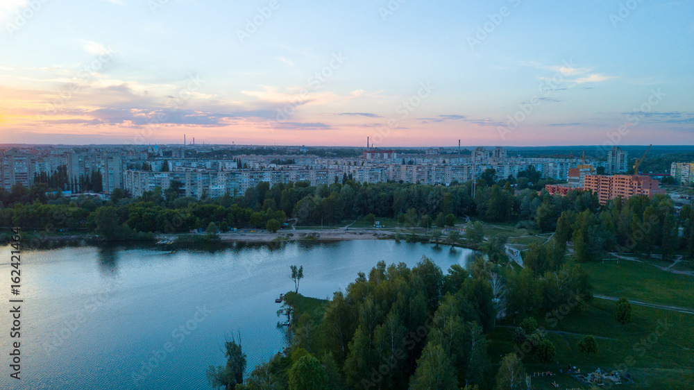 Flying over the trees and lake in the city at dawn - aerial photo