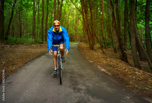 Fototapeta Naklejka Na Ścianę i Meble -  Middle-aged man is riding a road bike along a forest road