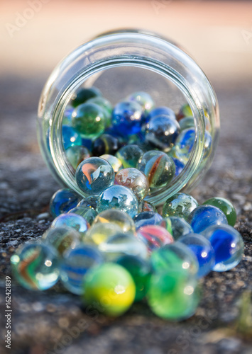 Glass jar full of crushers, fallen on the street. Front view of jar.
Bright picture, with blue as main color.
Front and background blurred.
Other colors red, green, yellow.