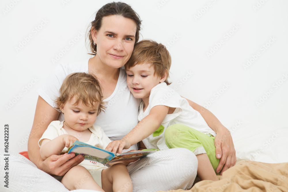 mother reads the book to two of her children the book in a bed. The happy family spends time together at home.

