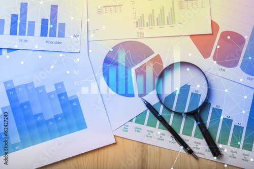 Fotografie Magnifying glass and documents with analytics data lying on table,selective focu