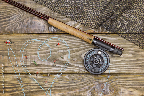 Fly rod , flies and landing net lying on an old wooden table. Cord drawn I love fly fishing.