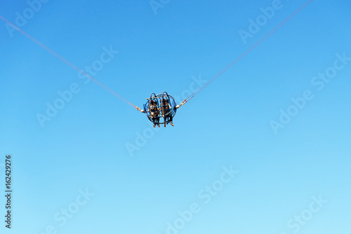 Two people on a catapult cage in amusement park against blue sky.