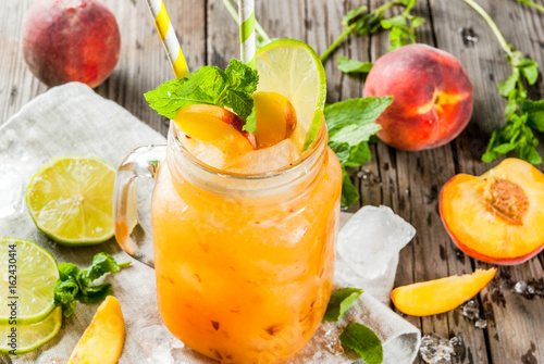 Summer drinks, cocktails. Vegan food. Peach smoothies, juice or lemonade. In a mason jar, with lime, chopped ice and mint leaves. On an old rustic wooden table with ingredients. Copy space