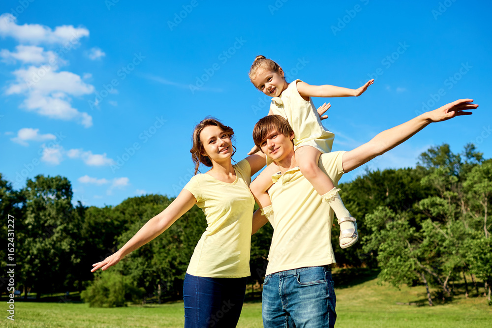 Fototapeta premium Happy family smiling in the park. Mother, father and daughter in nature on background of blue sky and trees.