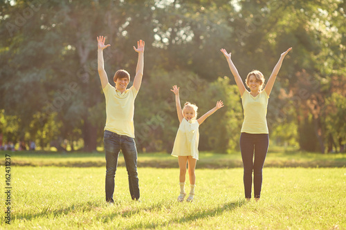 Happy family in park with hands up. Mother, father and daughter on green grass in nature.