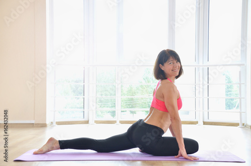 Portrait of a beautiful mature woman siting in yoga pose at the gym