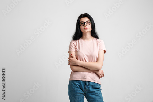 Portrait of smart beautiful brunette girl in eyeglasses with natural make-up, on grey background.