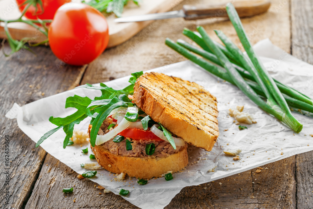 Toast sandwich with tuna, tomato, onion and arugula. Traditional healthy food made of fish, vegetables and grilled bread. Toast sandwich with tuna, tomato, onion and arugula. Traditional healthy food made of fish, vegetables and grilled bread.