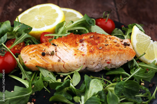 baked salmon grilled pepper lemon on a plate with lettuce leaves and tomato on wood background - healthy eating concept