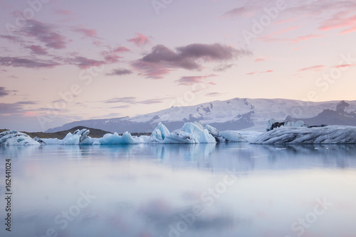 Giant pieces of ice flowing on and reflecting in cold lake with a huge glaciar behind, jokulsarlon glaciar lagoon, Iceland