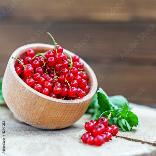 Juicy red currants in a wooden bowl. Useful berries and mint. The concept is healthy food, vitamins, diet and vegetarianism.
