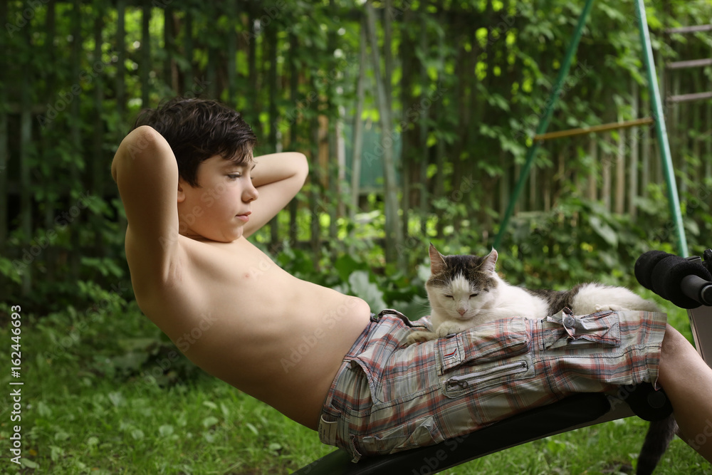 Obraz premium teenager boy make push up stomach exercise work out with cat on portable trainer outdoor summer photo