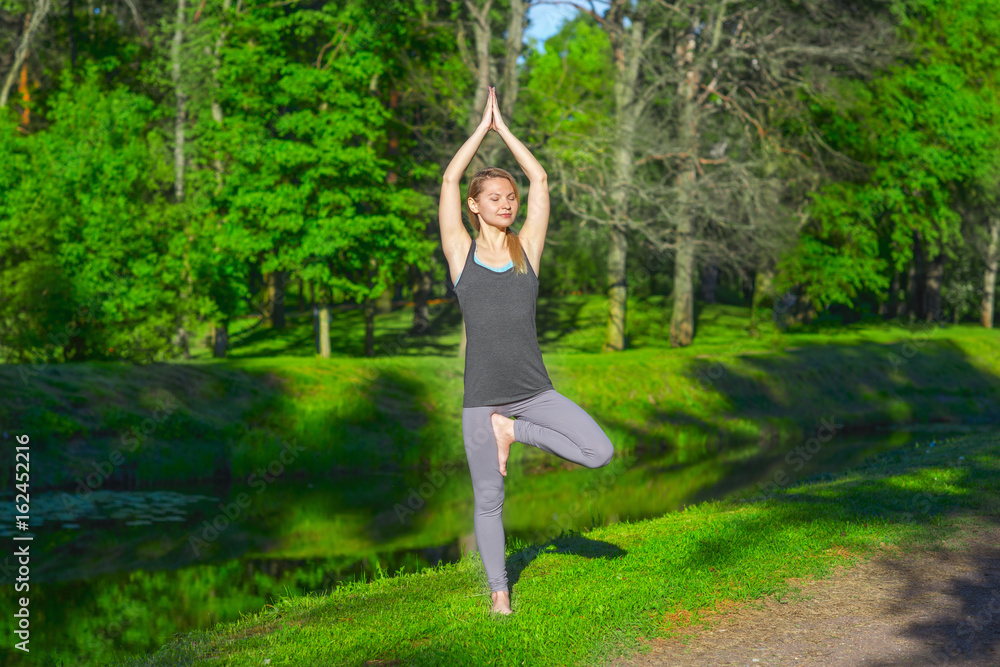 Young blonde woman exercising yoga Tree pose in the park