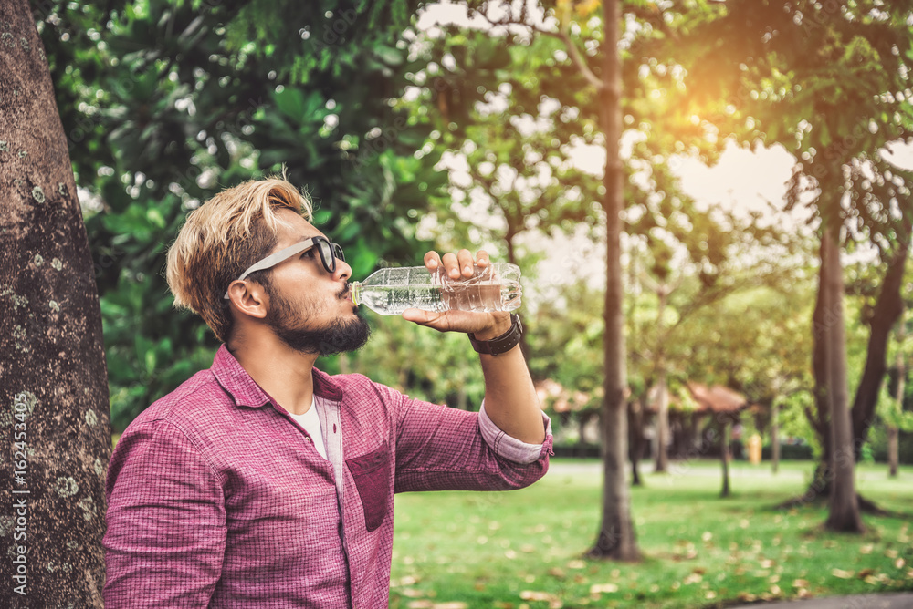 Young Hipster Man Drinking Water from Bottle after Traveling in Summer - Lifestyle Concept Young Hipster Man Drinking Water from Bottle after Traveling in Summer - Lifestyle Concept