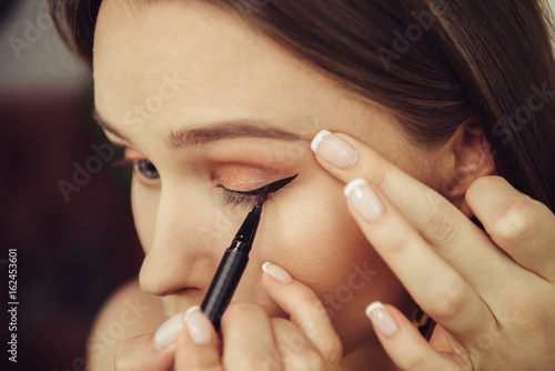 Tableau sur toile Woman doing makeup and painting black arrows