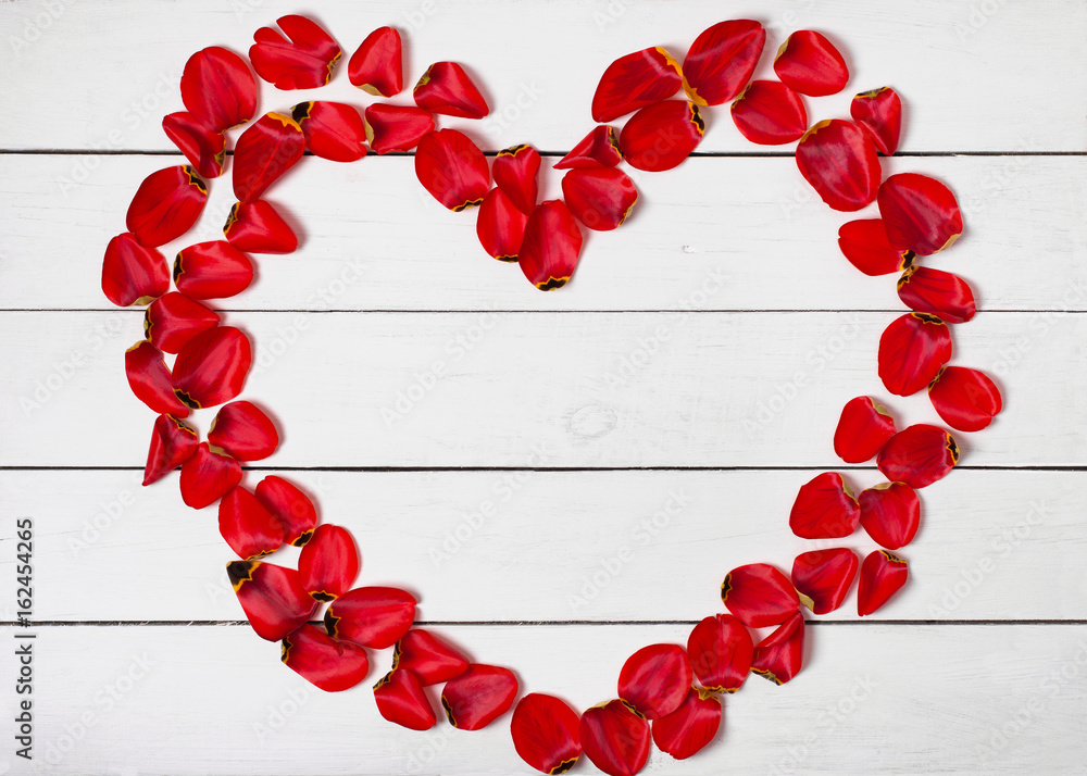 Obraz premium heart shape frame of red petals on white wooden table background