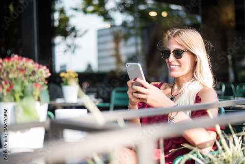 Wallpaper Mural Happy blonde beautiful woman using a mobile phone drinking a cup of coffee in a terrace Torontodigital.ca
