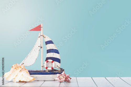 Antique sail boat Toy model with Ship'wheel, rope and seashell on white and blue wooden background - Nautical background