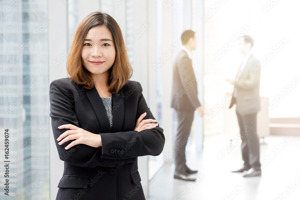 Asian businesswoman standing and crossing her arms in office building hallway Asian businesswoman standing and crossing her arms in office building hallway