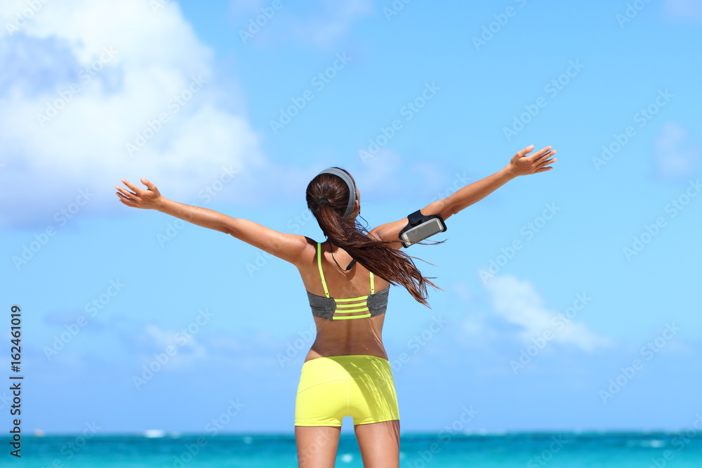 Fitness healthy lifestyle runner exercise success. Happy woman running with open arms in freedom listening to music with earphones and smartphone armband on blue copy space sky. Fitness healthy lifestyle runner exercise success. Happy woman running with open arms in freedom listening to music with earphones and smartphone armband on blue copy space sky.