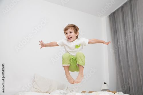 Cheerful little boy  jumping on bed at home. photo