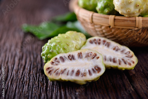 whole and half cut fresh noni fruit with leaf on wooden background
