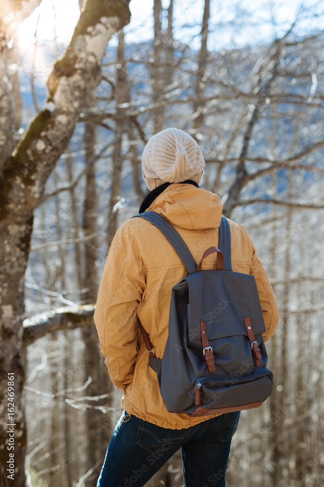 Hiker man with backpack and sleeping bag walking in the mountains in winter at sunset time. Enjoying the nature concept.