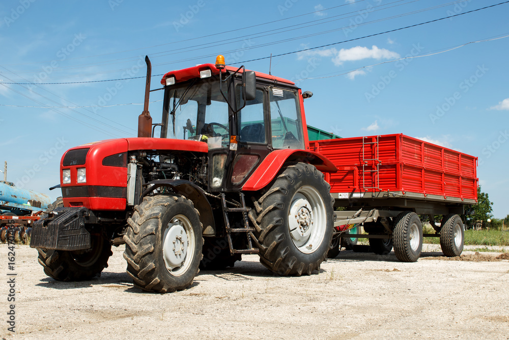 Fototapeta premium Red tractor with trailer parked on a farmyard