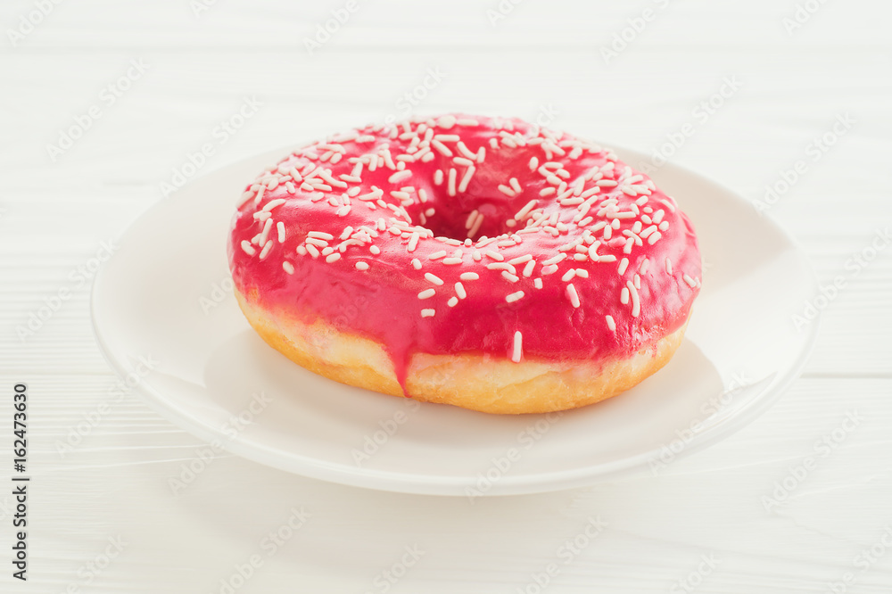 One pink donut, close-up. Donut on a plate on white wooden table. Delicious breakfast, sweet donut with copy space. One pink donut, close-up. Donut on a plate on white wooden table. Delicious breakfast, sweet donut with copy space.