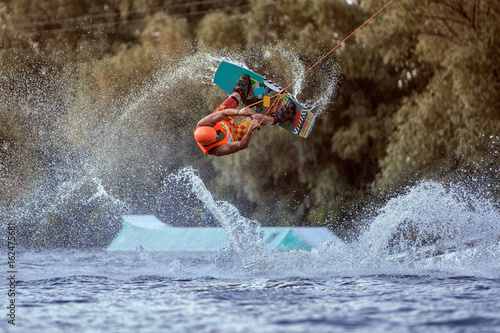 Man makes an extreme jump on wakeboarding, around there are a lot of splashes and splashes of water. This is an extreme sport.