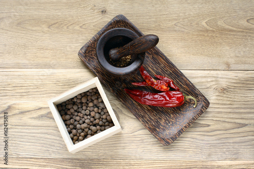Hot red pepper and allspice with pounder and pestle on wood background