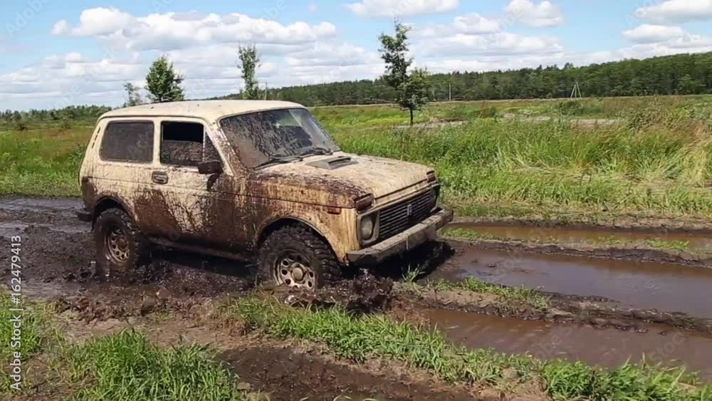 Dirty and mud-splattered car is driving through the mud on a bad country dirt-road Dirty and mud-splattered car is driving through the mud on a bad country dirt-road