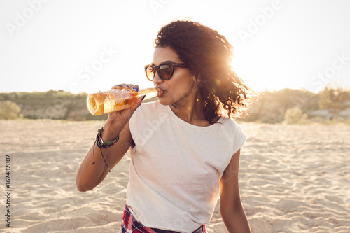 Wall Mural Young pretty african girl in sunglasses drinking beer
