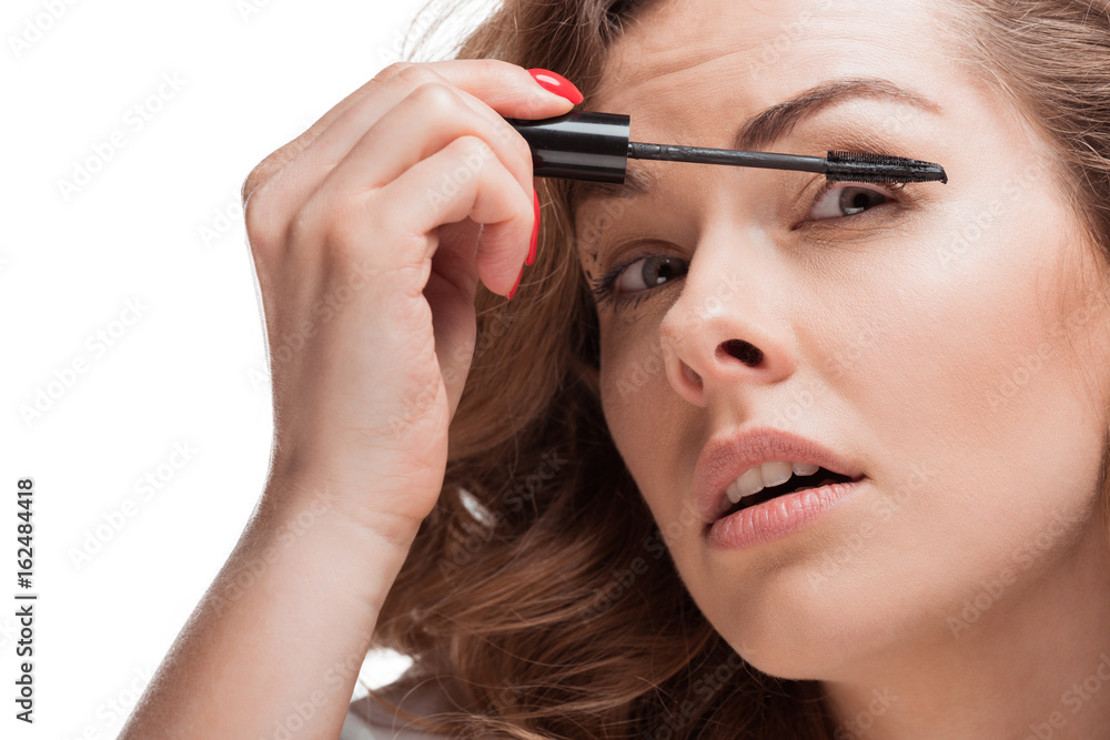 head shot of focused woman applying mascara isolated on white